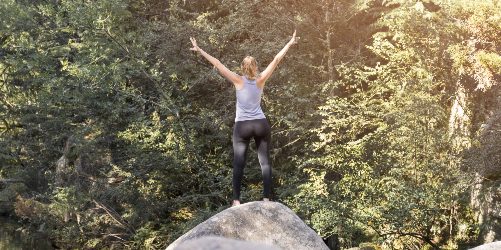 CrossFit Rising Star Woman with arms raised on a Bolder looking at a forest